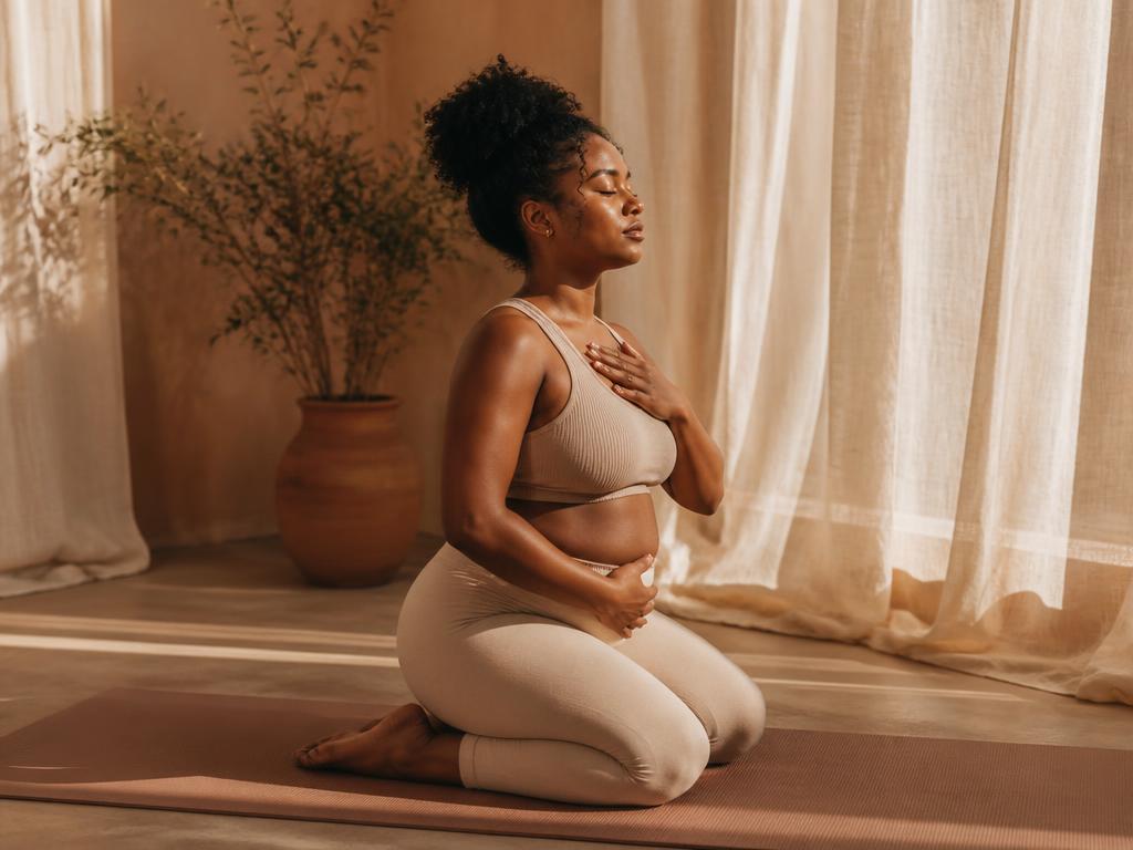 Black woman early postpartum kneeling on a mat practicing core breathing in a sunlit studio
